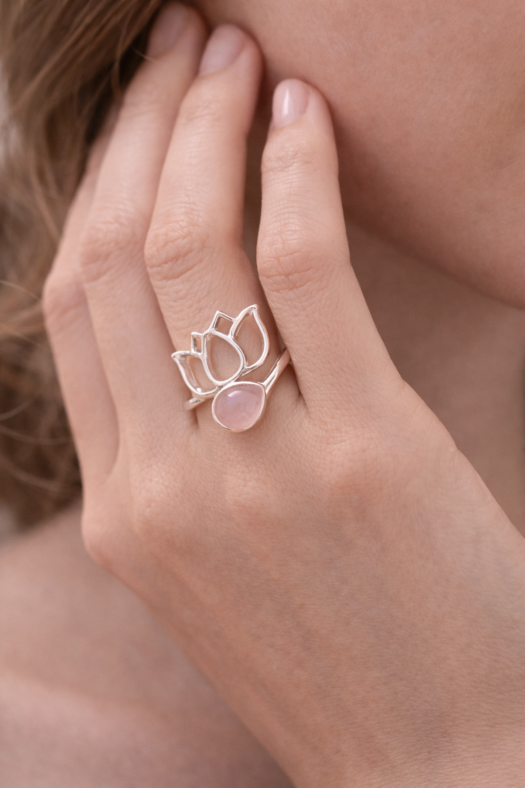 Anneau lotus en argent 925 avec pierre rose quartz, porté sur une main féminine, près du visage.