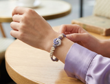 Bracelet Mandala Fleur de Pêcher Blanc et Violet, tissé et ajustable autour du poignet, posé près d’une table.