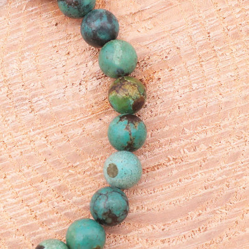 Bracelet en turquoise du Tibet avec perles rondes vert-bleu sur bois clair, vue en gros plan.