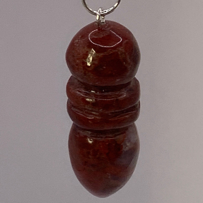 Pendule Egyptien en Jaspe Rouge montre une petite forme cylindrique et arrondie, en jaspe rouge, suspendue par un anneau.